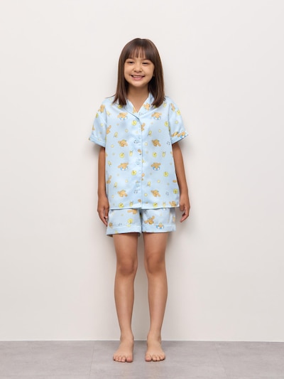 A girl wearing the girls satin pajama set (short-sleeve top and shorts) with Sanrio character print, standing against a plain background.