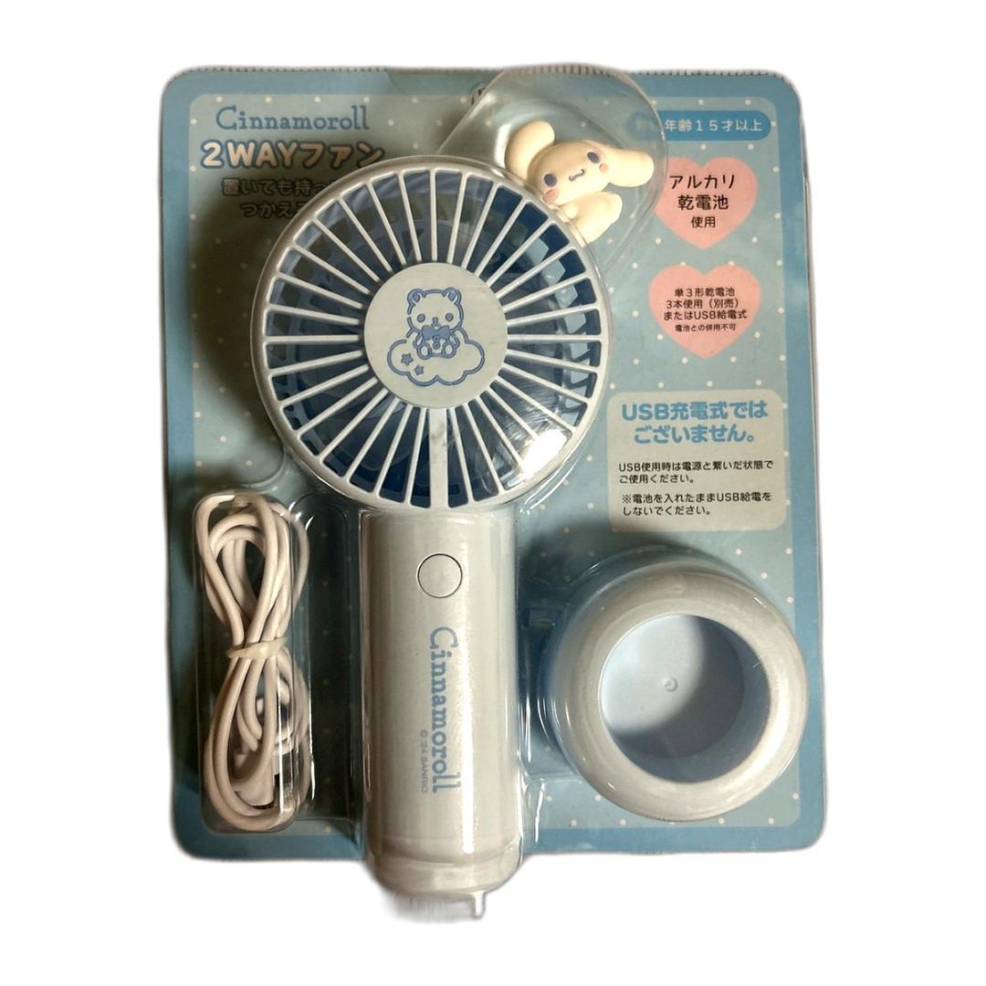 Packaged light-blue Cinnamoroll 2-way handheld fan with USB cable and round base visible.