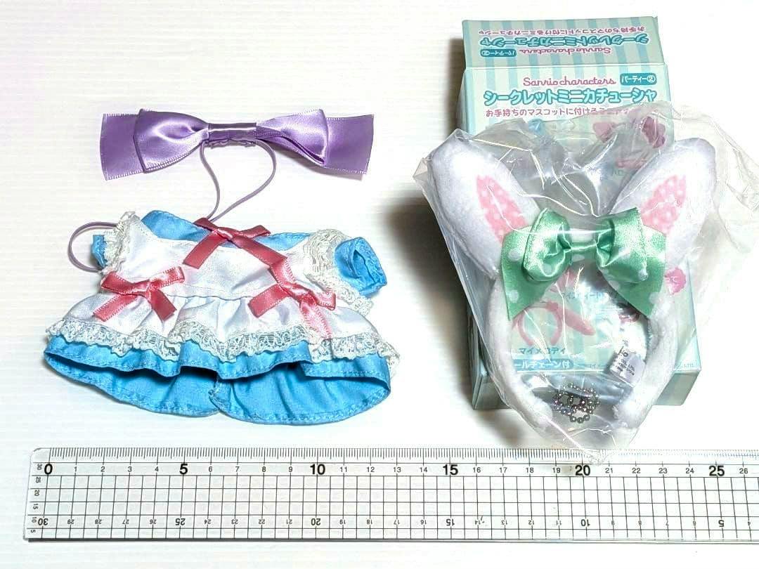 A blue-and-white doll dress with pink bows, a purple ribbon headband, and a packaged white bunny-ear mini headband with a green bow arranged on a white background with a ruler.
