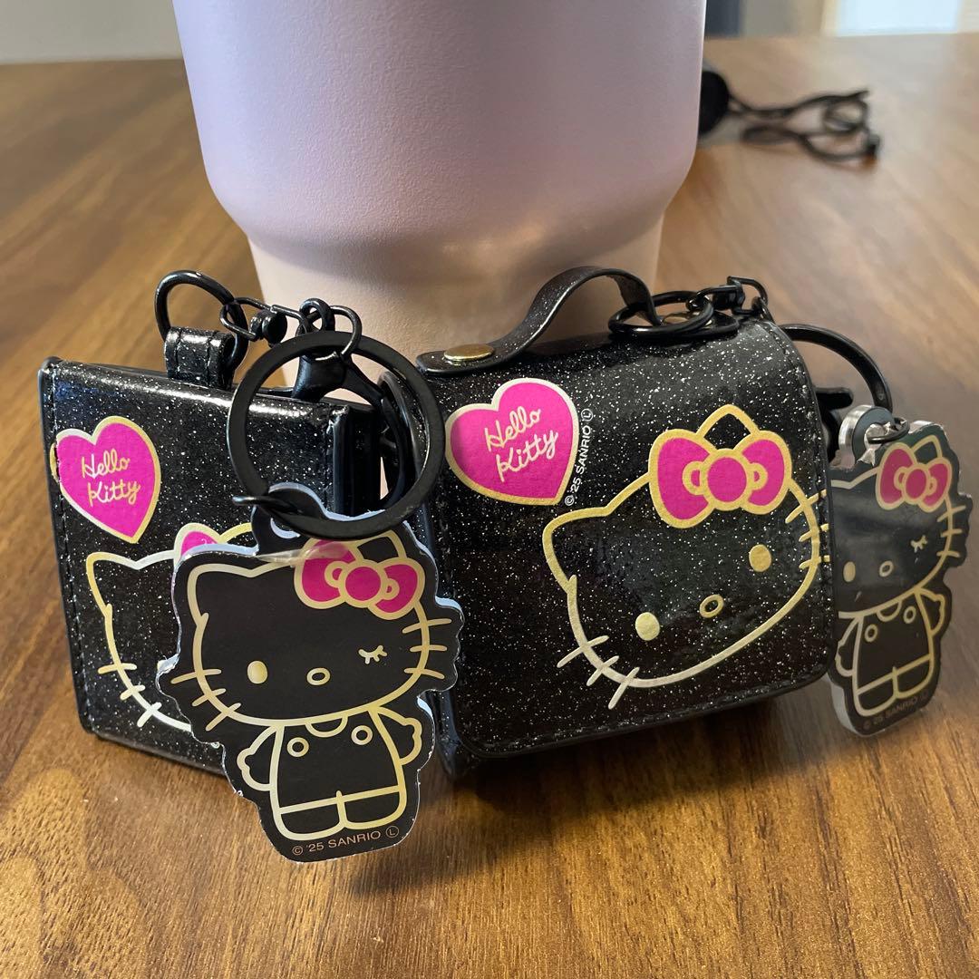 Two black glitter Hello Kitty compact mirror cases with Hello Kitty keychain charms sitting on a wooden table.