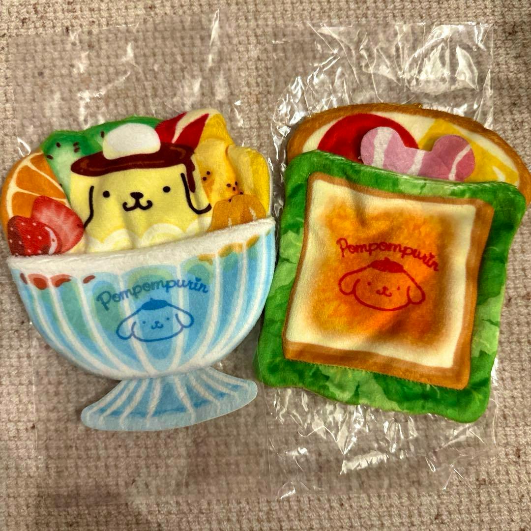 Two Sanrio Pompompurin secret mascot pockets: a blue-striped dessert-cup pocket holding a pudding plush and a green toast-shaped pocket.