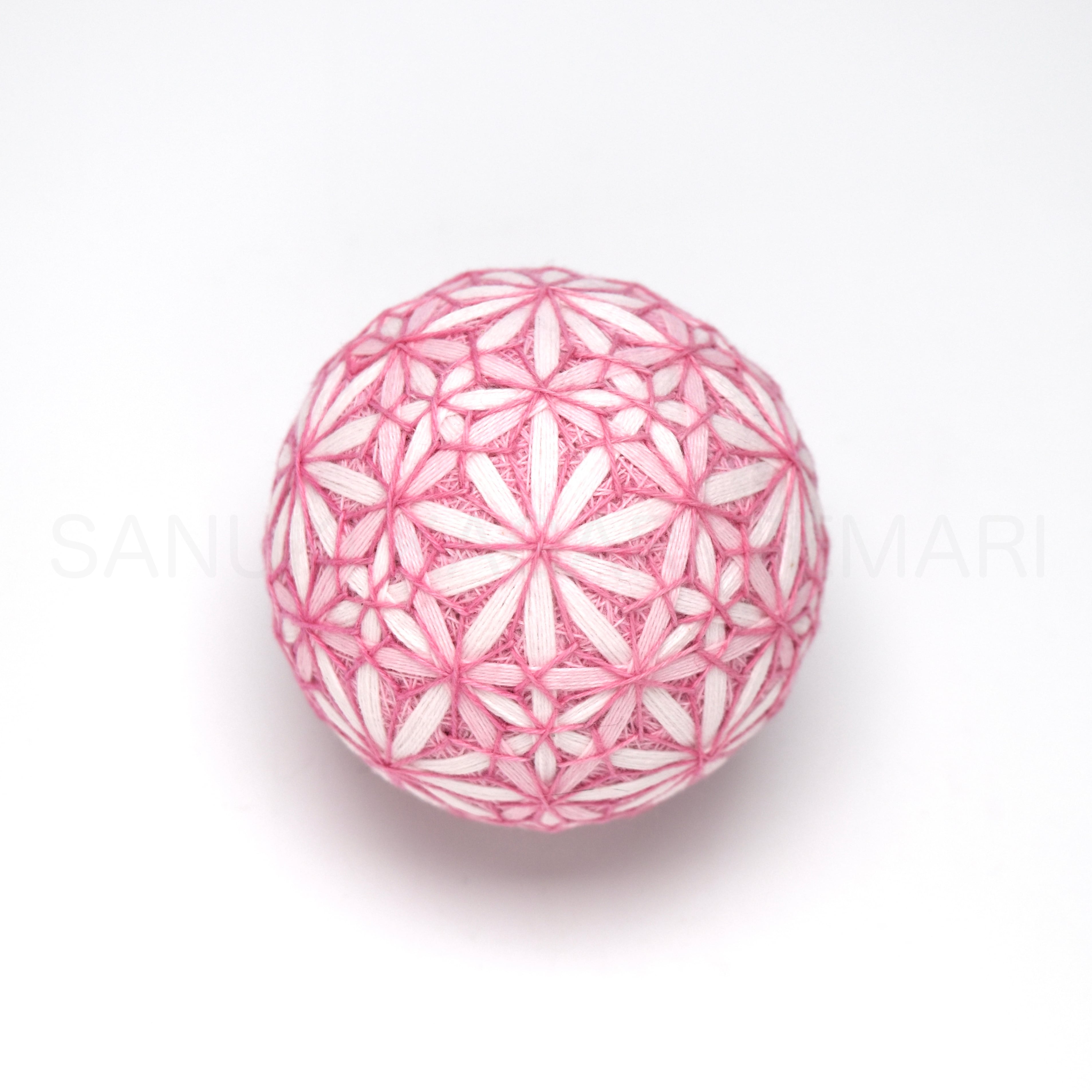 Pink and white embroidered temari ornament (讃岐かがり手まり「七宝麻の葉」) on a white background.