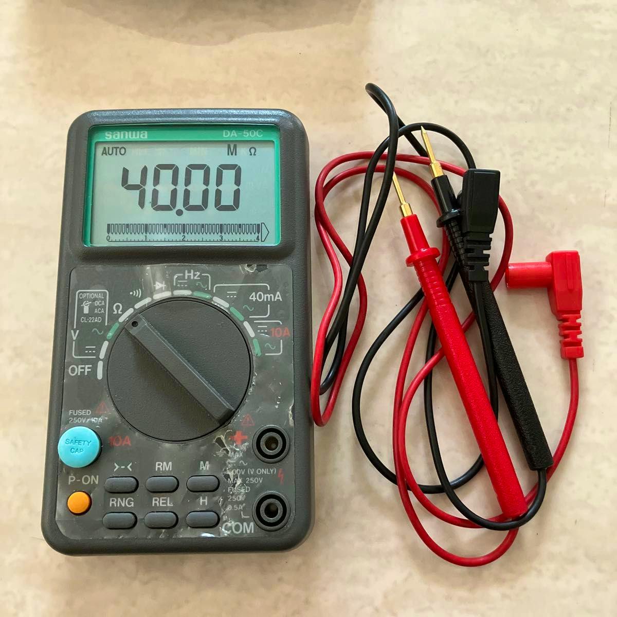 Sanwa DA-50C digital multimeter with its red and black test leads coiled beside it on a light surface.