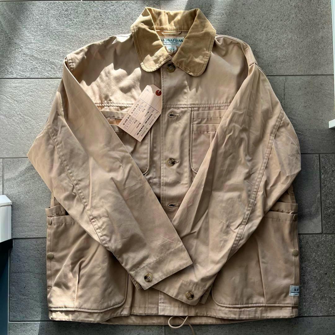 Beige SASSAFRAS Overgrown Warden men's cotton jacket laid flat showing the front with collar, buttons, and pockets.