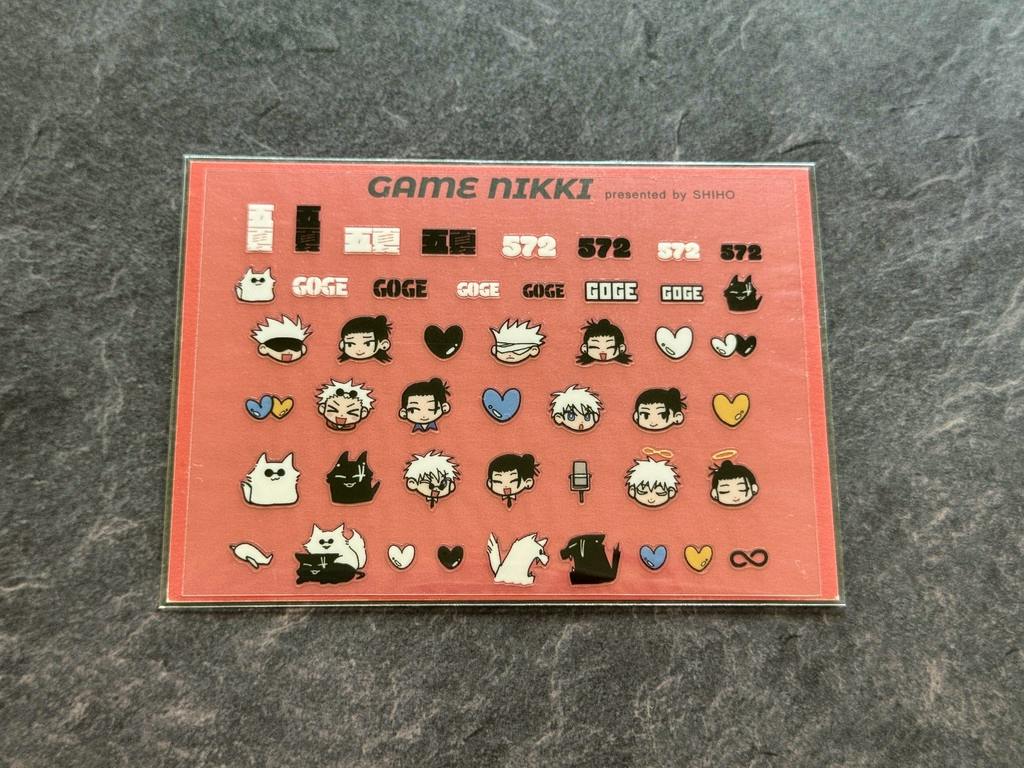 Rectangular sheet of nail stickers on a pink background showing small cartoon faces, cats, hearts, and text designs.