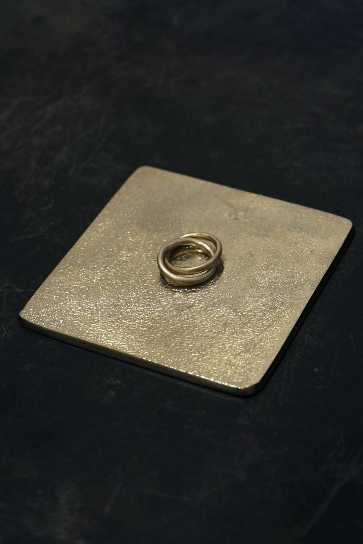 A silver ring displayed on a textured square metal plate against a dark background.