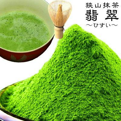 Bright green matcha powder piled on a dish beside a prepared bowl of matcha and a bamboo whisk.