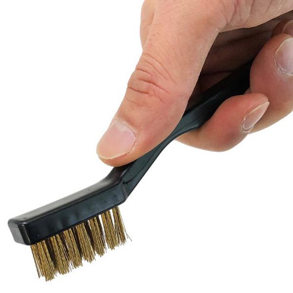 A small wire cleaning brush with metal bristles and a black handle held in a hand.