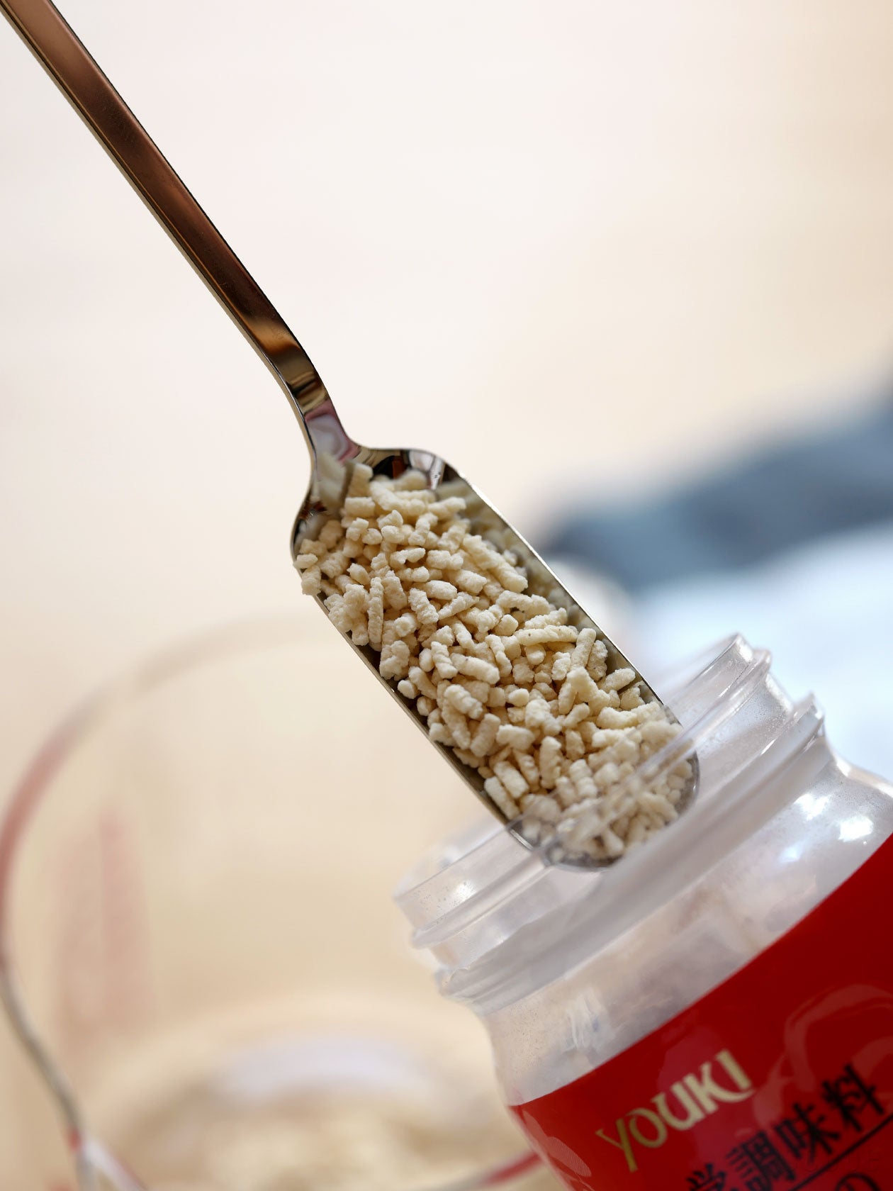 A metal small teaspoon (cani spoon) holding granular seasoning over an open jar.