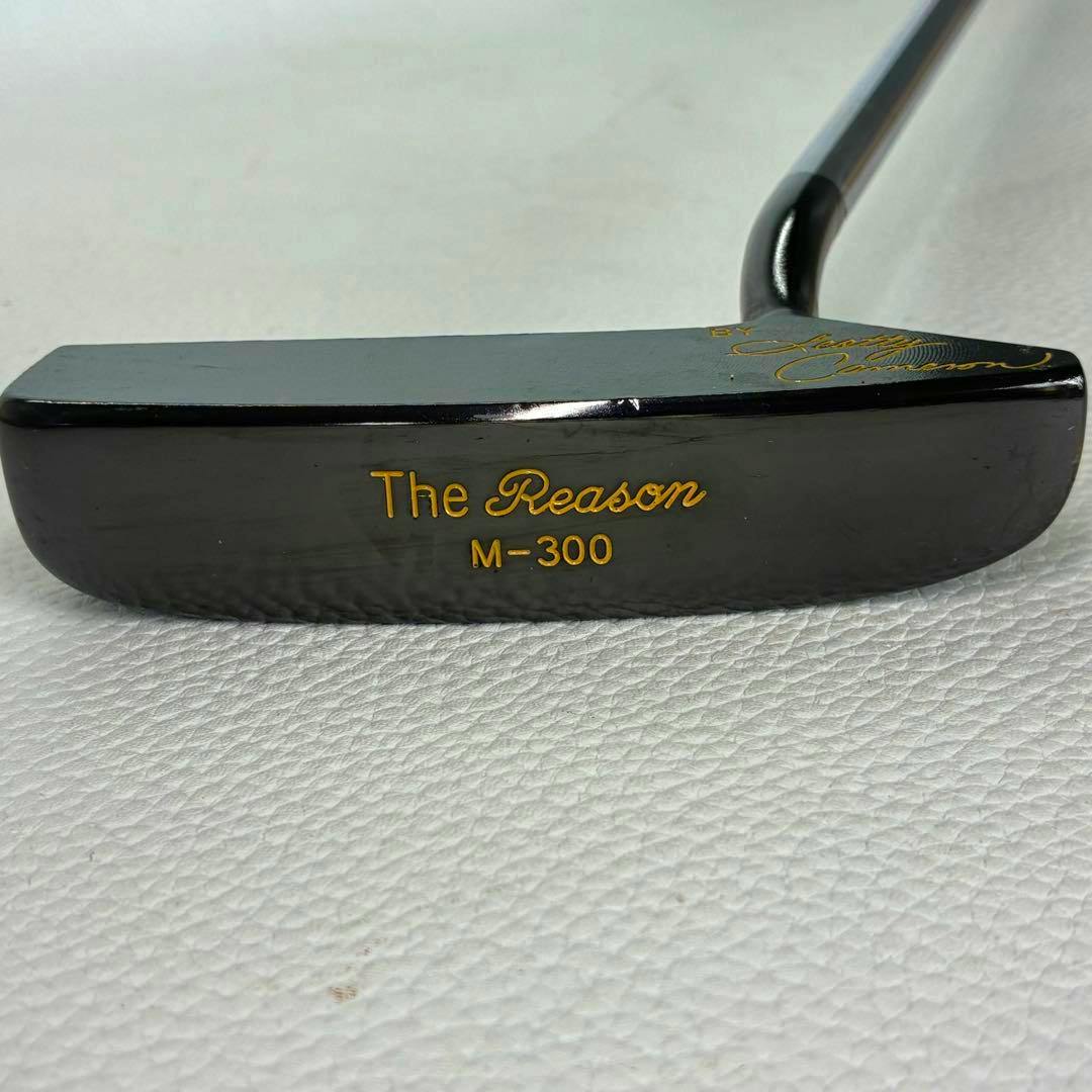 Close-up of the golf putter head showing the engraved gold text "The Reason M-300".