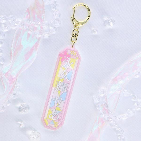 Photograph of the acrylic keychain お名前キーホルダー【永久輝せあ】 showing the pastel geometric name tag with the text 永久輝せあ and a gold clasp on a light fabric background.