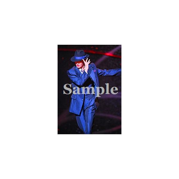 Stage photograph showing a performer in a blue suit and fedora mid-performance with a 'Sample' watermark.