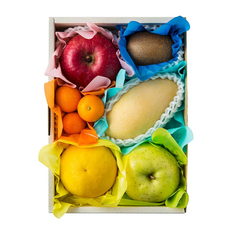 Top-down photo of a boxed assortment of seasonal fruits (about 4–5 types) wrapped in colorful protective paper.