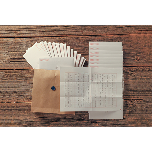 A letter set arranged on a wooden surface showing multiple envelopes, unfolded and folded sheets with printed text, and a button-seal envelope.