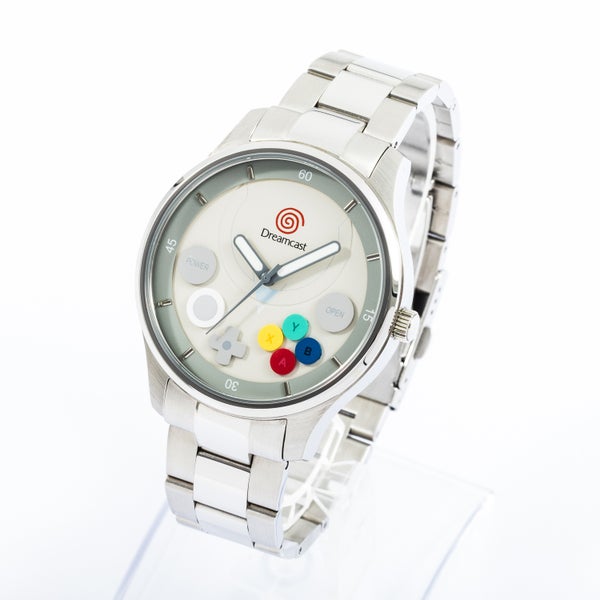 Silver metal-cased wristwatch with a Dreamcast logo and colored controller-button motifs on the dial, shown on a metal bracelet.