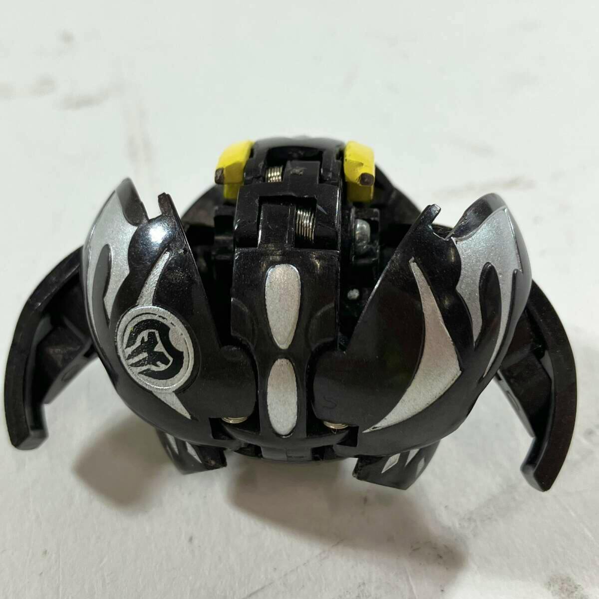 Black and silver Bakugan figure (破ムニキスS デスムニキス) partially opened showing metal parts and yellow accents.