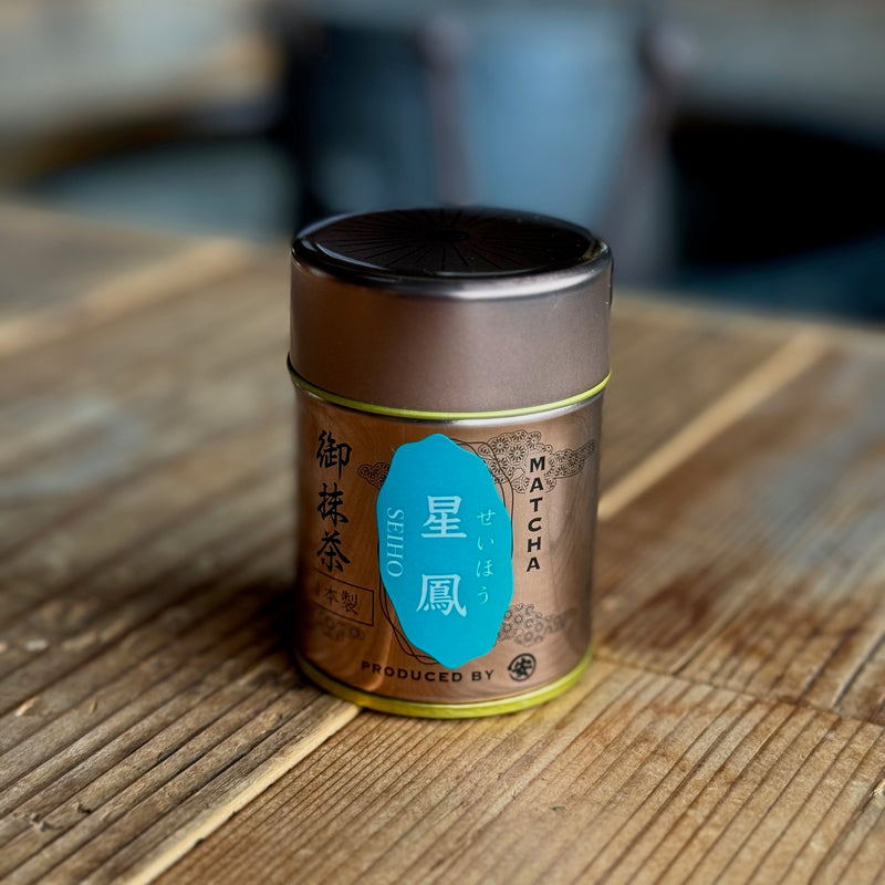 A small metal tin of matcha labeled “星鳳 SEIHO” placed on a wooden surface.