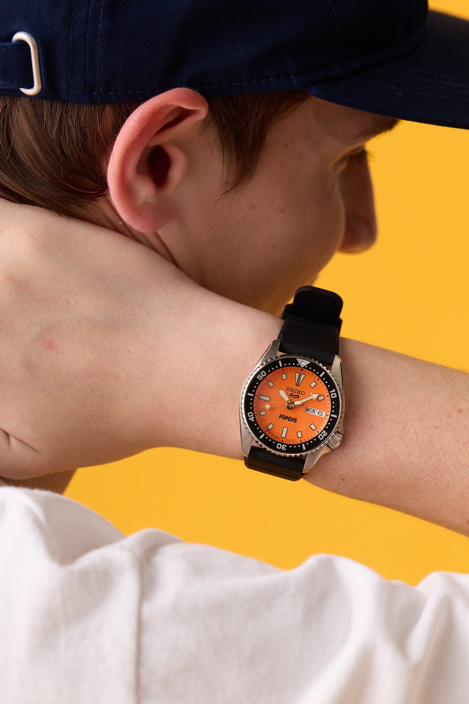 Close-up of the SEIKO 5 SPORTS × POPEYE SKX "Orange Boy" watch with an orange dial on a person's wrist.