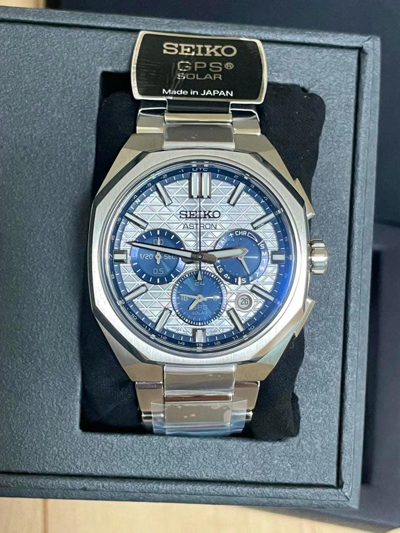 Close-up of the Seiko Astron wristwatch with a white patterned dial, blue subdials, and metal bracelet displayed in its box.