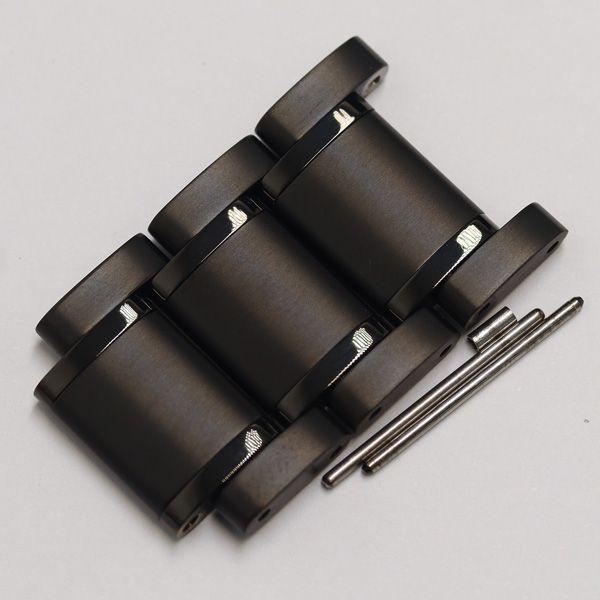 Three black metal watch bracelet links and two metal pins on a white background.