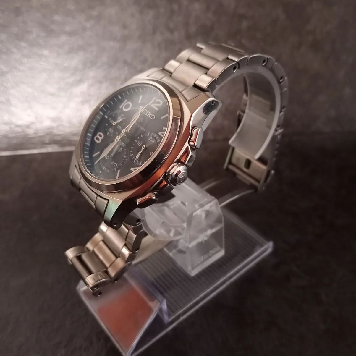 Silver Seiko Brightz chronograph wristwatch with a black dial shown on a clear display stand.