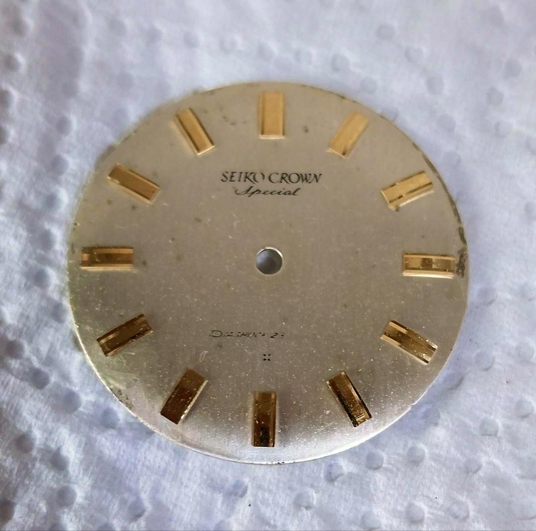 Front view of a SEIKO CROWN Special watch dial with gold hour markers and a central hole on a white textured background.