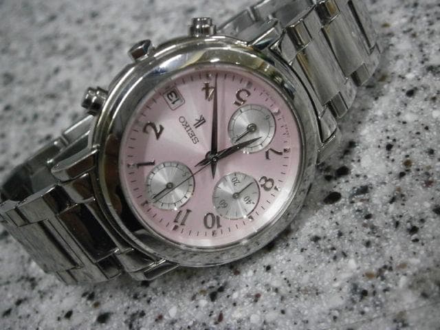 Seiko metal-cased chronograph wristwatch with a pink (sakura) dial and metal bracelet on a speckled surface.