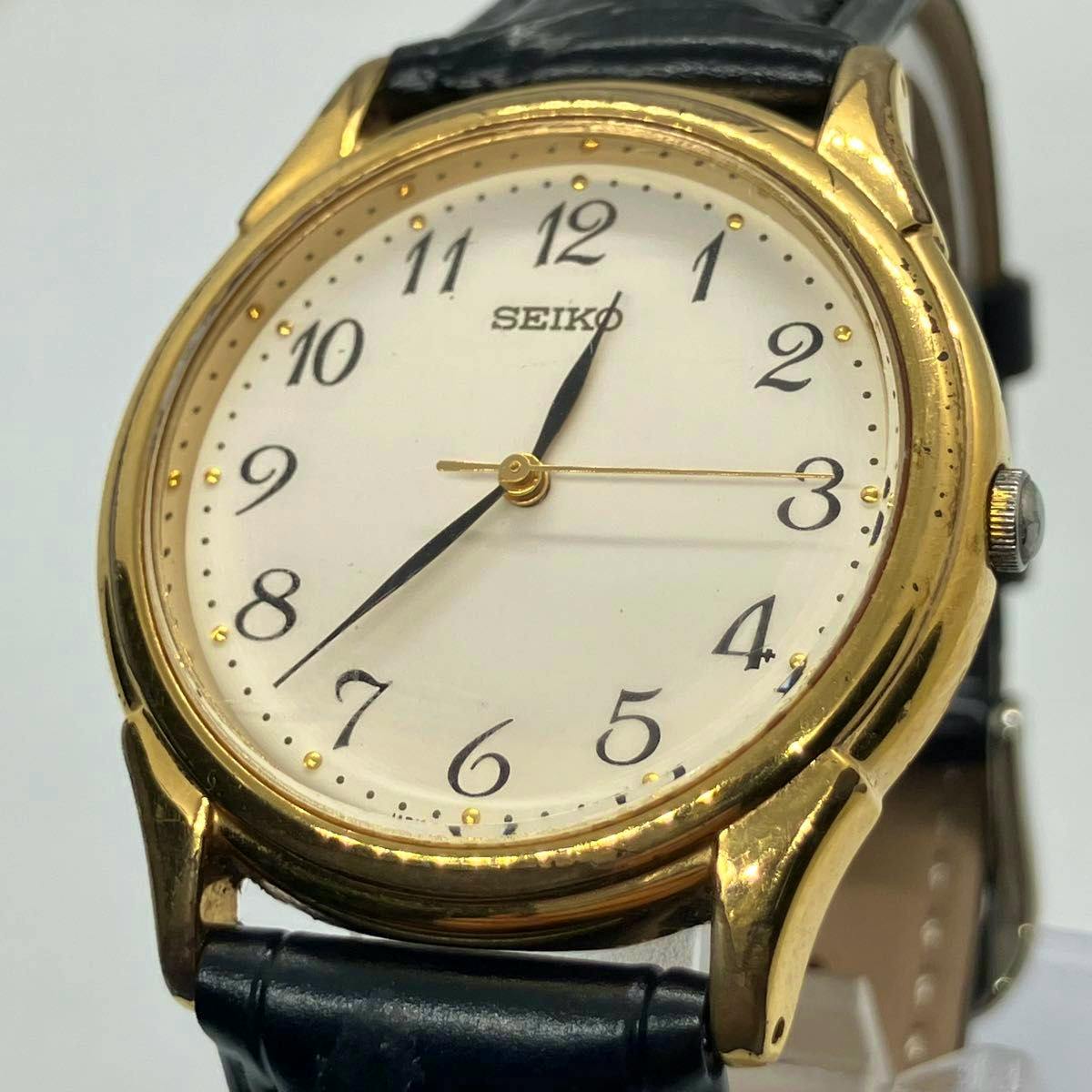 Close-up front view of a SEIKO men's quartz wristwatch with a gold metal case, white dial with Arabic numerals, and a black leather strap.