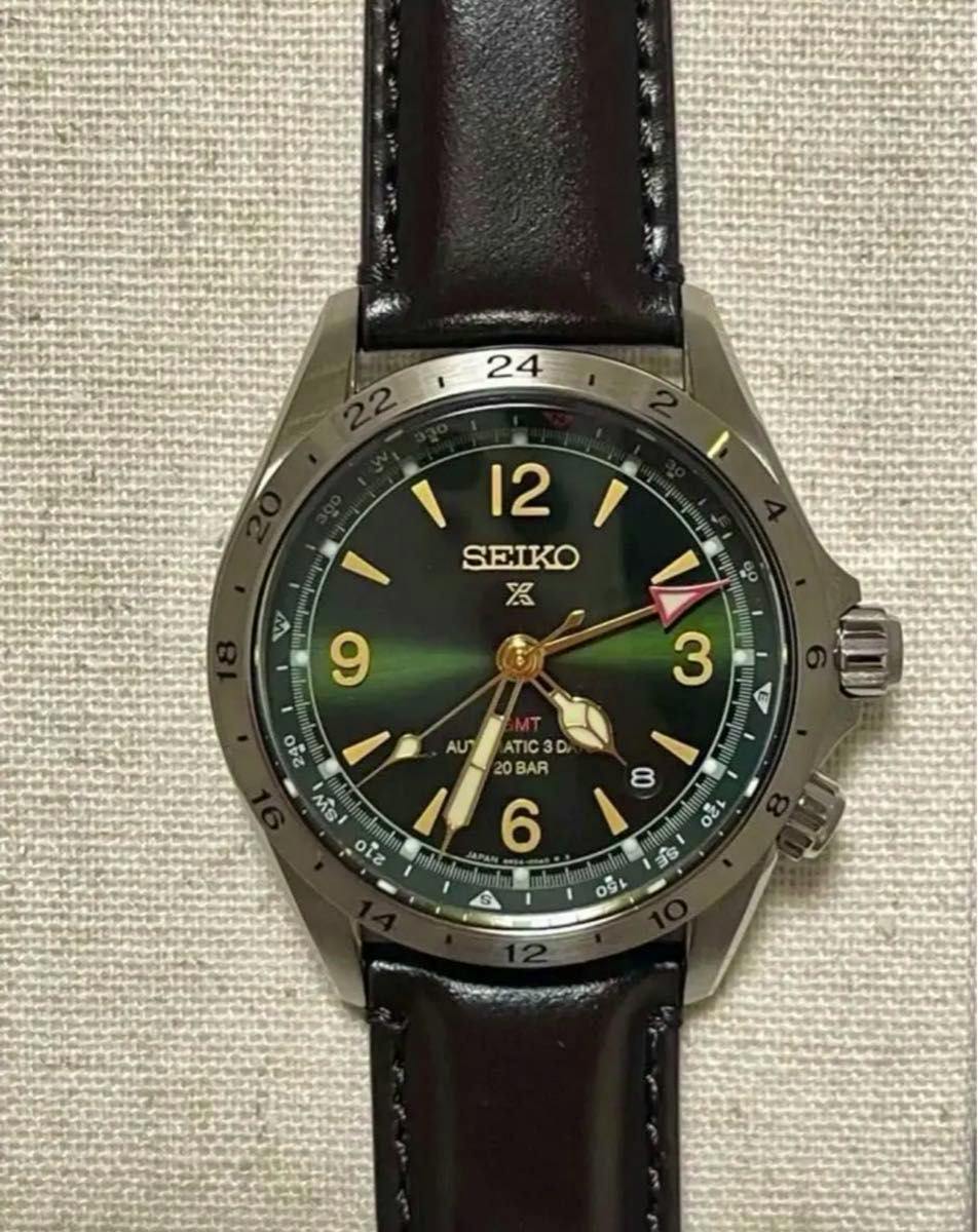 Close-up photo of the SEIKO SBEJ005 wristwatch showing a green sunburst dial with gold-tone numerals and hands, a metal bezel, and a black leather strap.