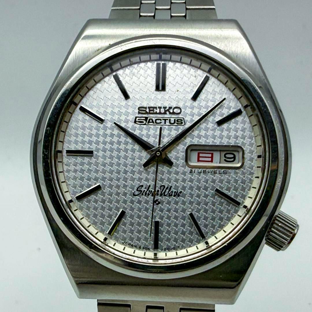Front-facing close-up of the Seiko Silver Wave metal-cased wristwatch showing the textured silver dial, hour markers, hands, and the day‑date window.