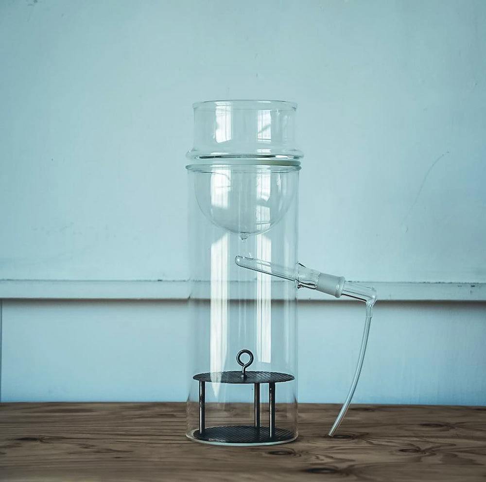 Assembled clear-glass household distiller on a wooden tabletop against a pale wall.