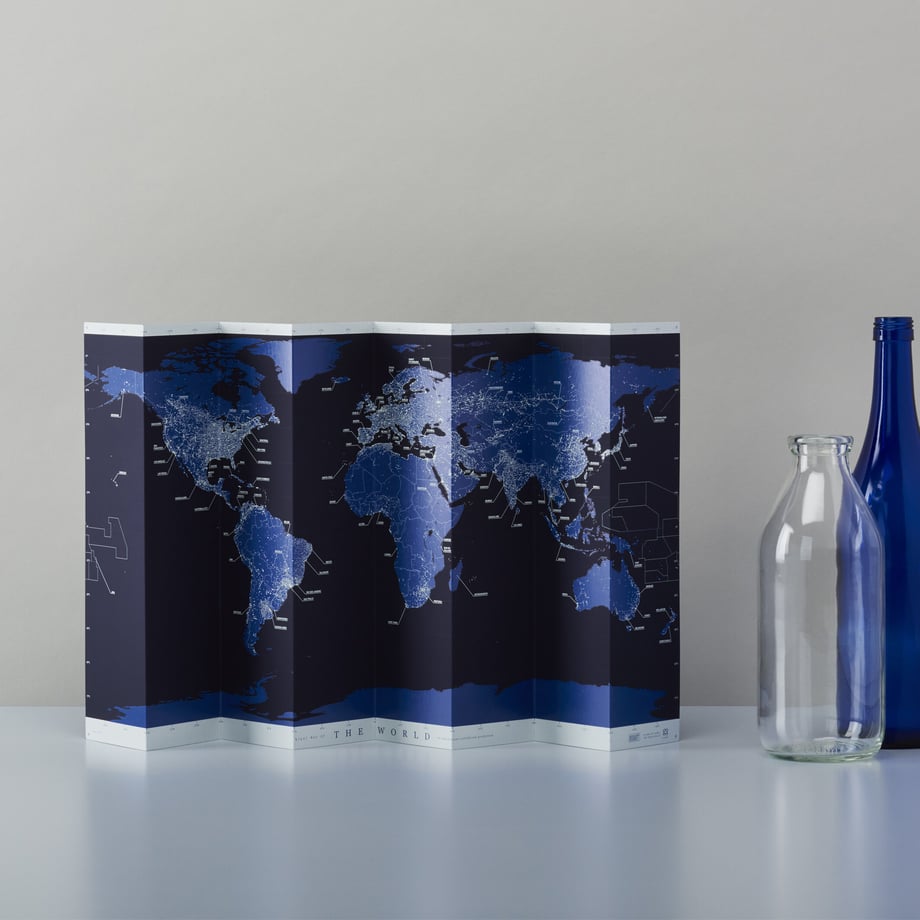 Folded night-color stand-alone world map displayed on a table next to two bottles.