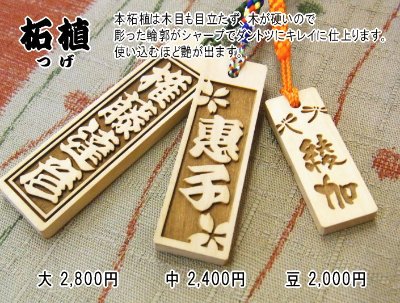 Close-up of three wooden senjafuda-style rectangular straps with carved Japanese characters and attached cords.