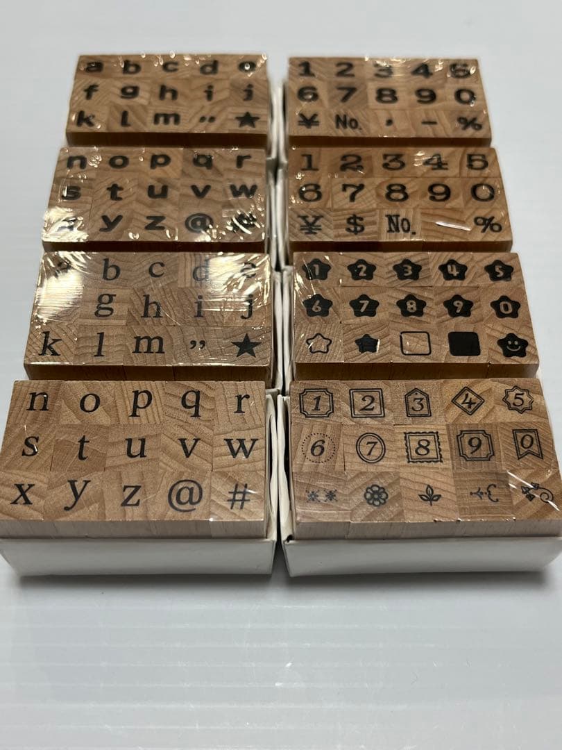 Eight wooden rubber stamps showing lowercase alphabet letters, numbers, and symbols arranged in two columns on a white surface.