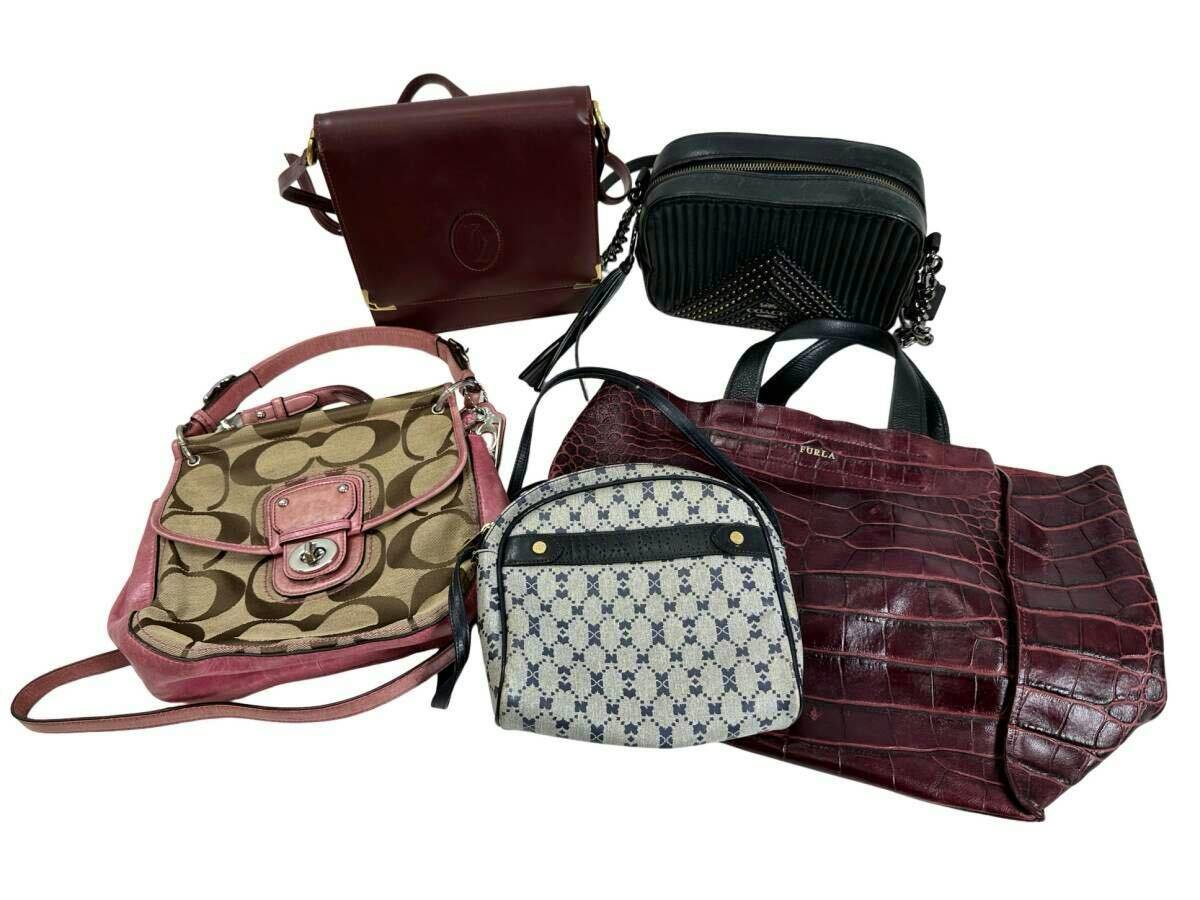 Five assorted handbags and shoulder bags, including a Coach canvas shoulder bag, arranged on a white background.