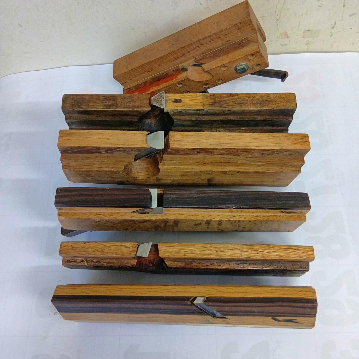 Six wooden planes laid flat on a white surface with their blades visible.