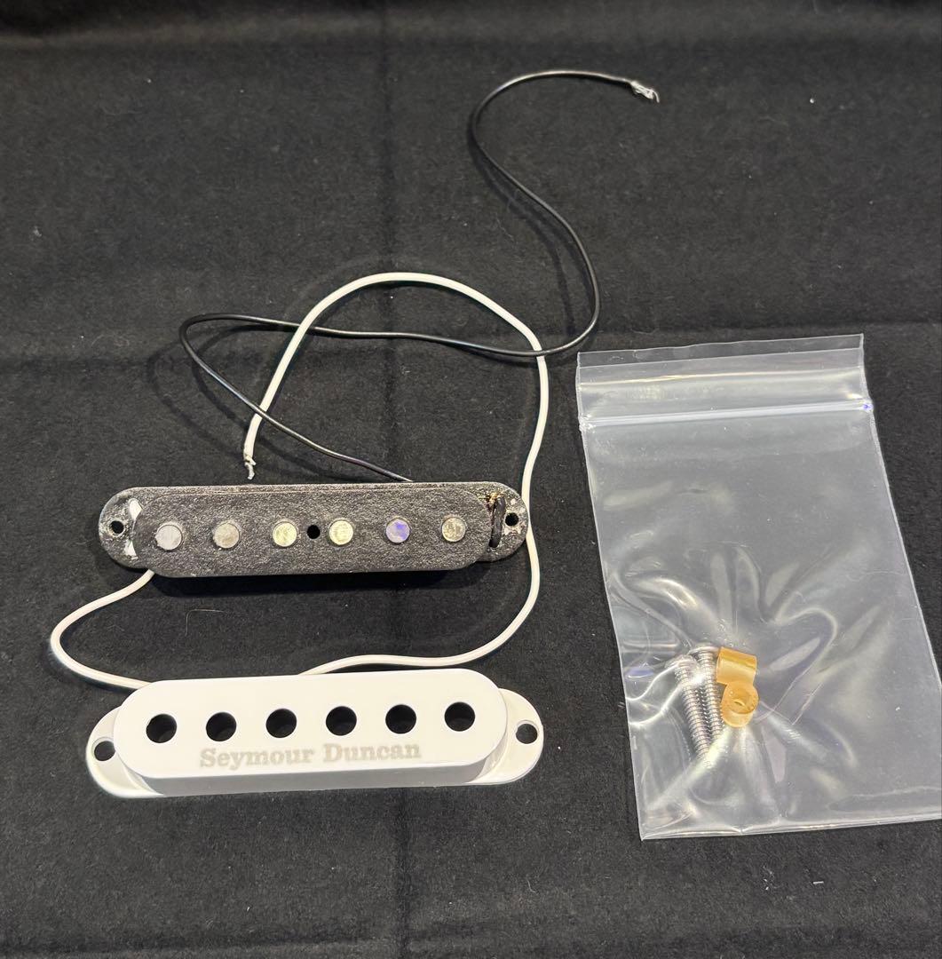 Two single-coil guitar pickups—one with a white cover and one with exposed pole pieces—plus mounting screws in a small plastic bag on a black background.