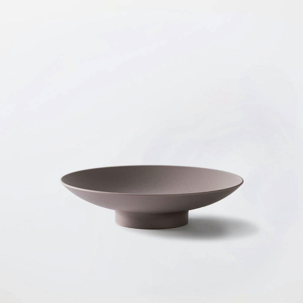 A grey shallow ceramic bowl on a short raised foot photographed on a white background.