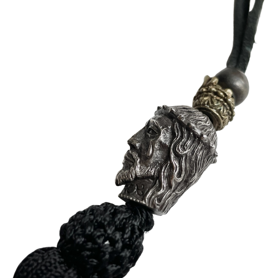Close-up of a silver Christ head pendant with a crown and attached black tassel on a cord.