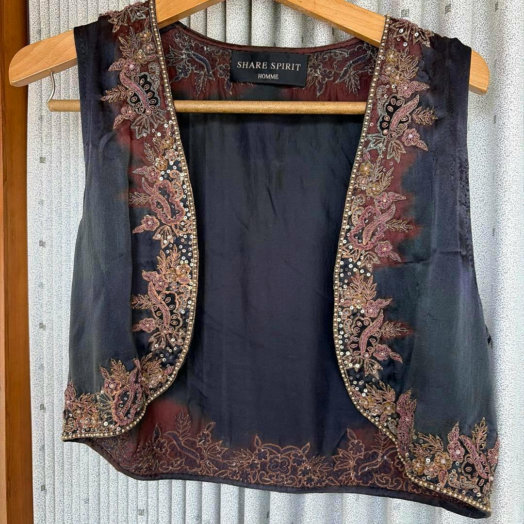 A SHARE SPIRIT HOMME silk embroidered vest hanging on a wooden hanger showing floral metallic embroidery along the front edges and hem.