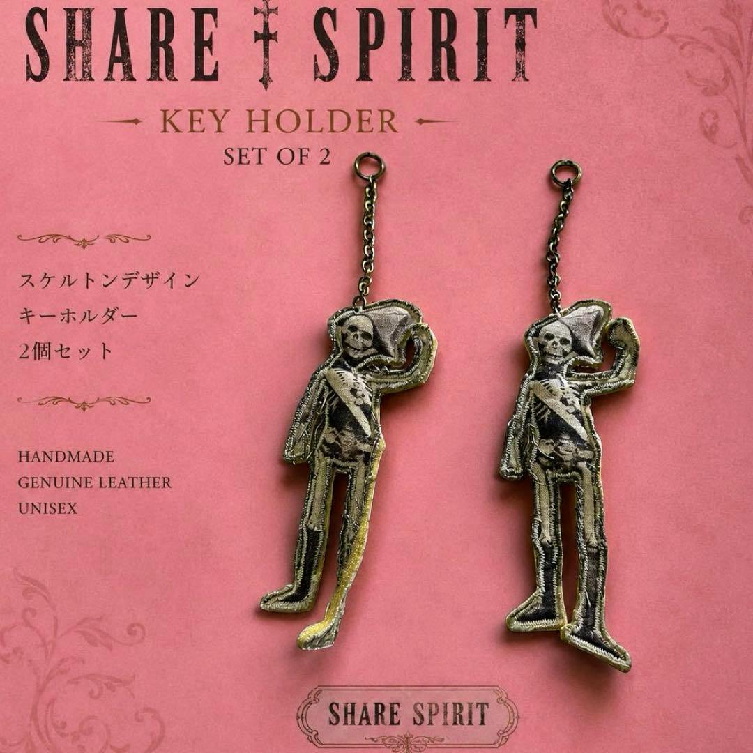 Two skeleton-shaped keychain charms hanging from short chains on a pink 'SHARE SPIRIT' backing card labeled "Key Holder Set of 2."