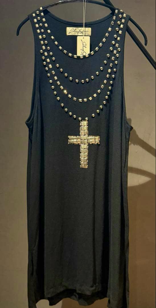 Black tank top hanging on a hanger with rows of metallic studs and a beaded cross design on the front.