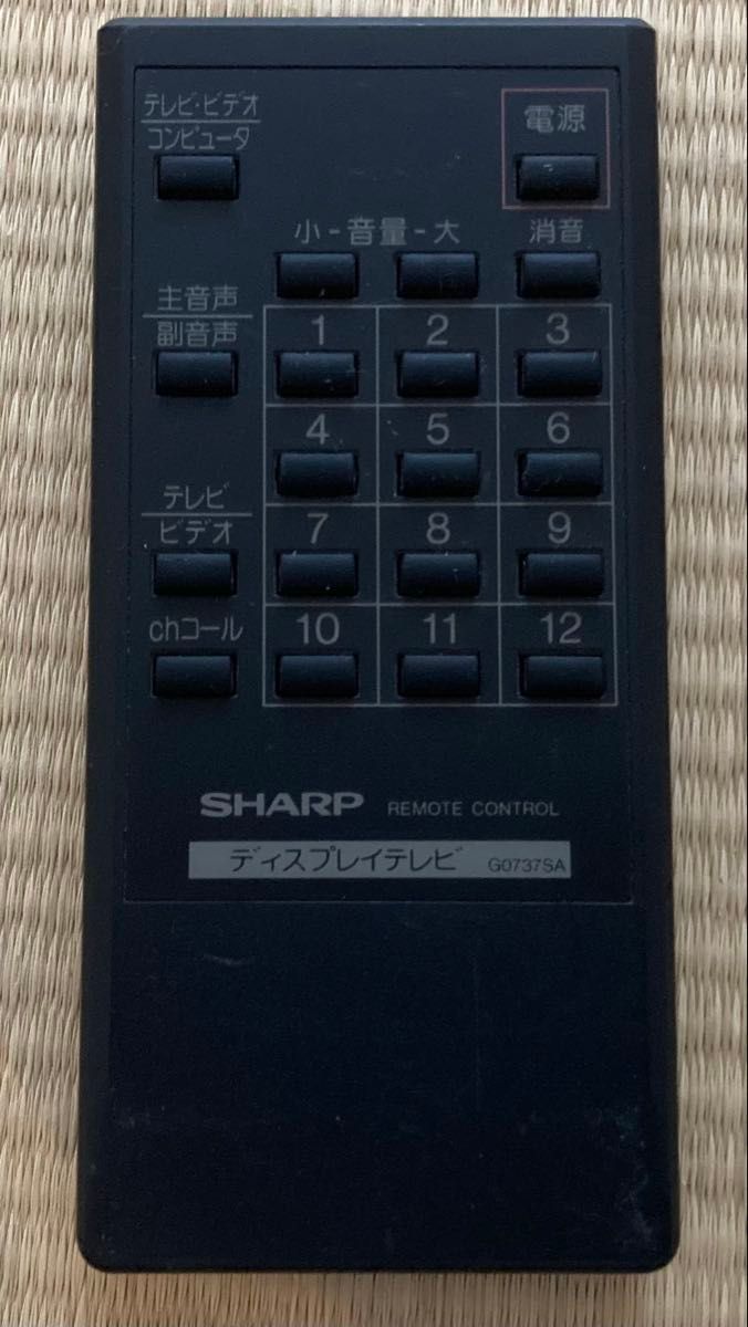 Front view of a black Sharp remote control for a display (X68000), showing numeric buttons, power button, and model label G0737SA.