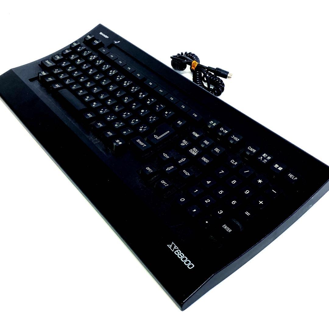Top-front perspective of a black SHARP X68000 keyboard showing keys, numeric keypad, and coiled cable.