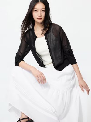 Model wearing the sheer short crew-neck cardigan over a white top and skirt.