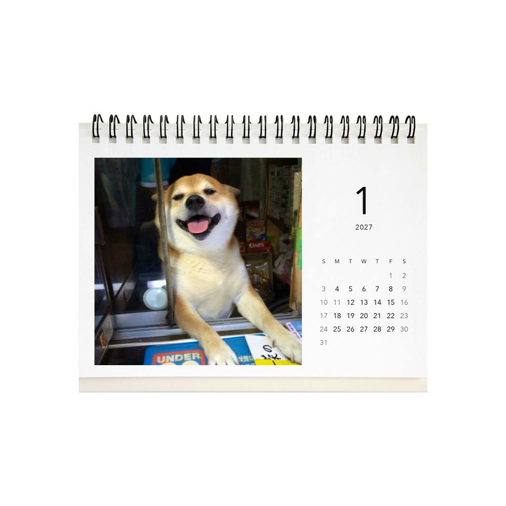 A spiral-bound desk calendar page for 2027 showing a smiling Shiba dog photo on the left and a monthly date grid on the right.