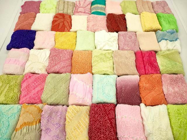 Array of folded obiage (kimono accessory) pieces in various colors and shibori patterns arranged in rows, shown as the product.