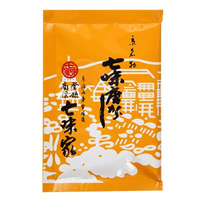 Front view of an orange packet of 七味唐がらし (shichimi togarashi) spice mix showing Japanese text and white decorative pattern.