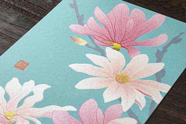 A postcard showing pink and white flowers with gold-accented centers on a blue background.