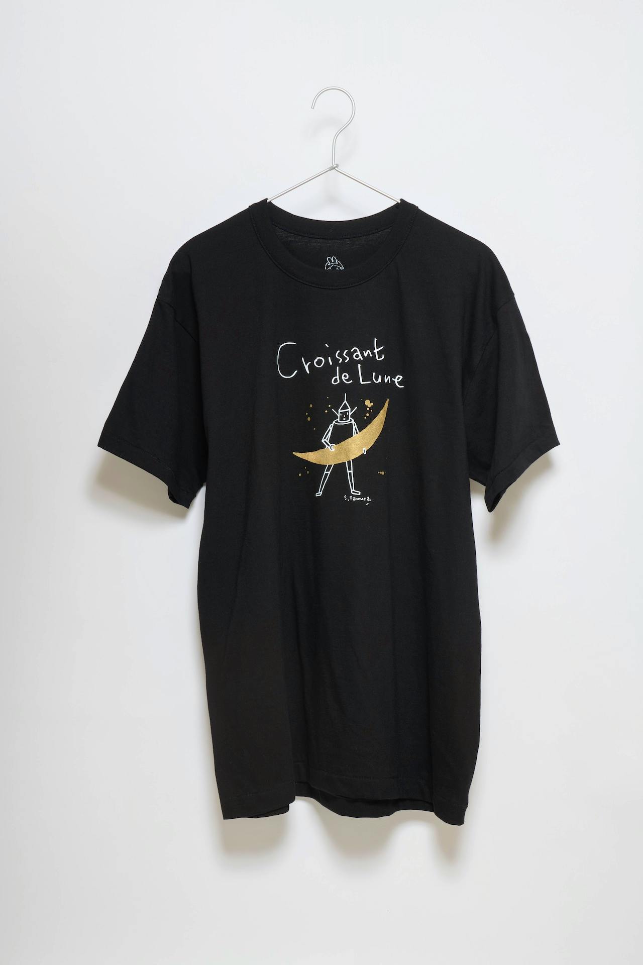 Black cotton T-shirt hung on a hanger showing a crescent-moon graphic and the text "Croissant de Lune."